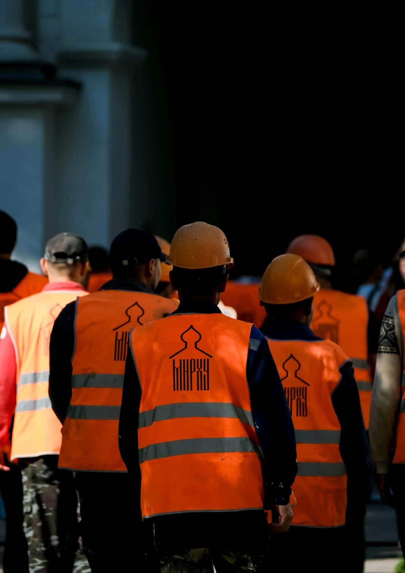 Groupe d'ouvriers de dos, en casque et gilet orange haute visibilité